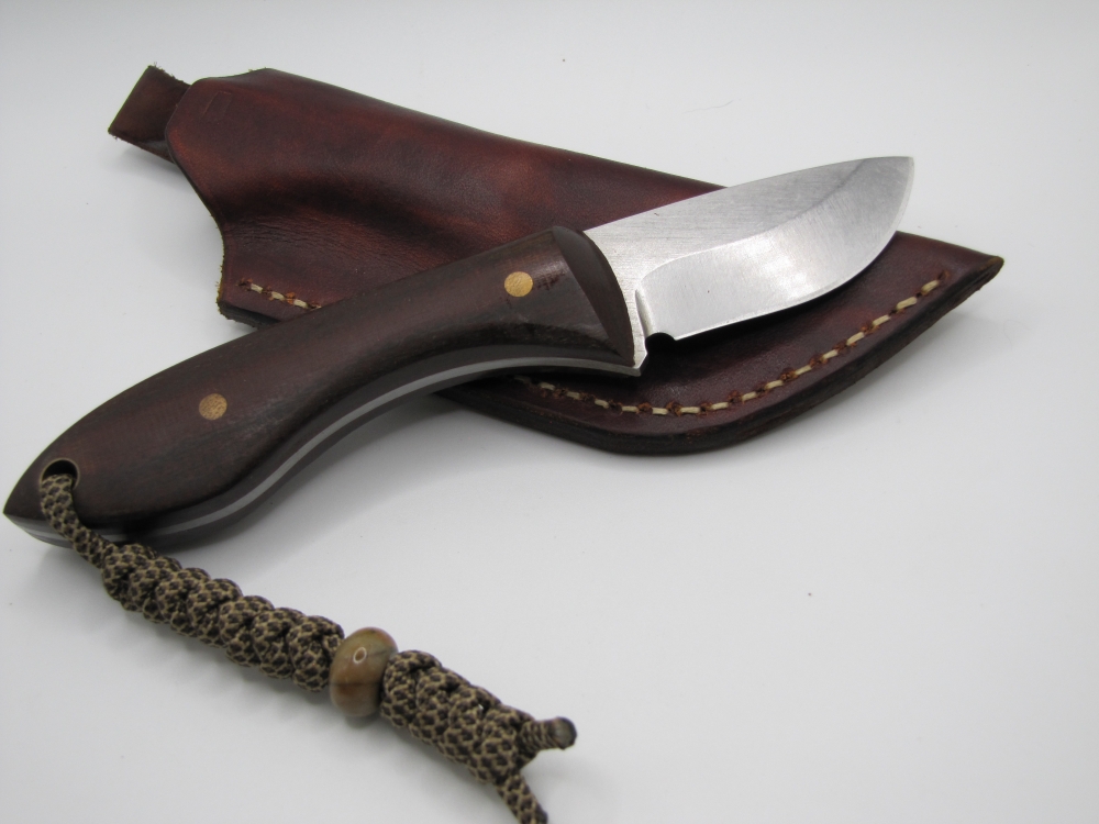 1095 high carbon drop point skinning knife with a red micarta handle with lanyard