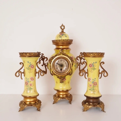 Garniture de cheminée ancienne de style baroque comprenant une pendule et une paire de bases de candélabres en céramique jaune à décor floral, montures en métal doré.
